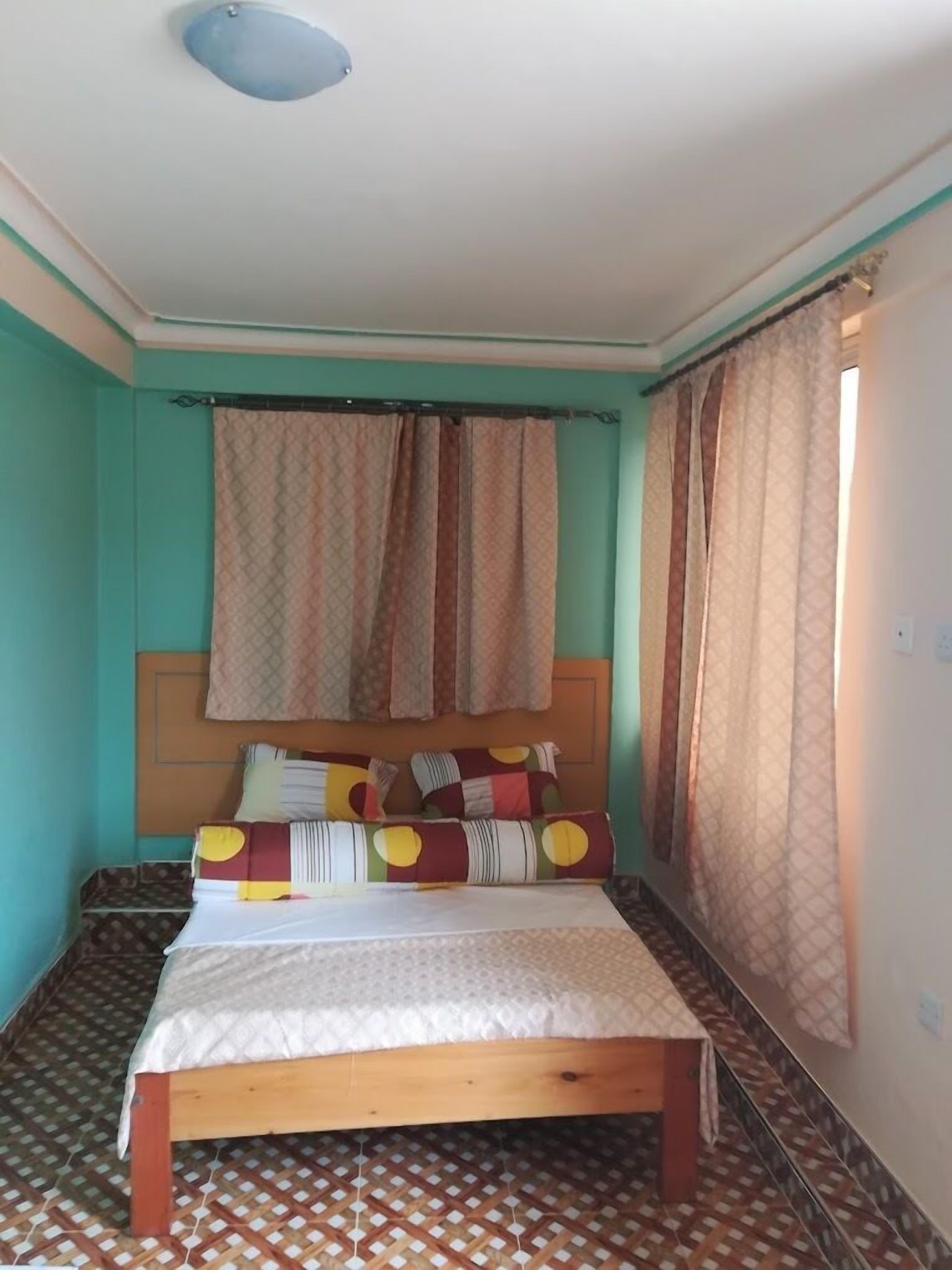 A bedroom with a bed, patterned curtains, and a patterned floor.