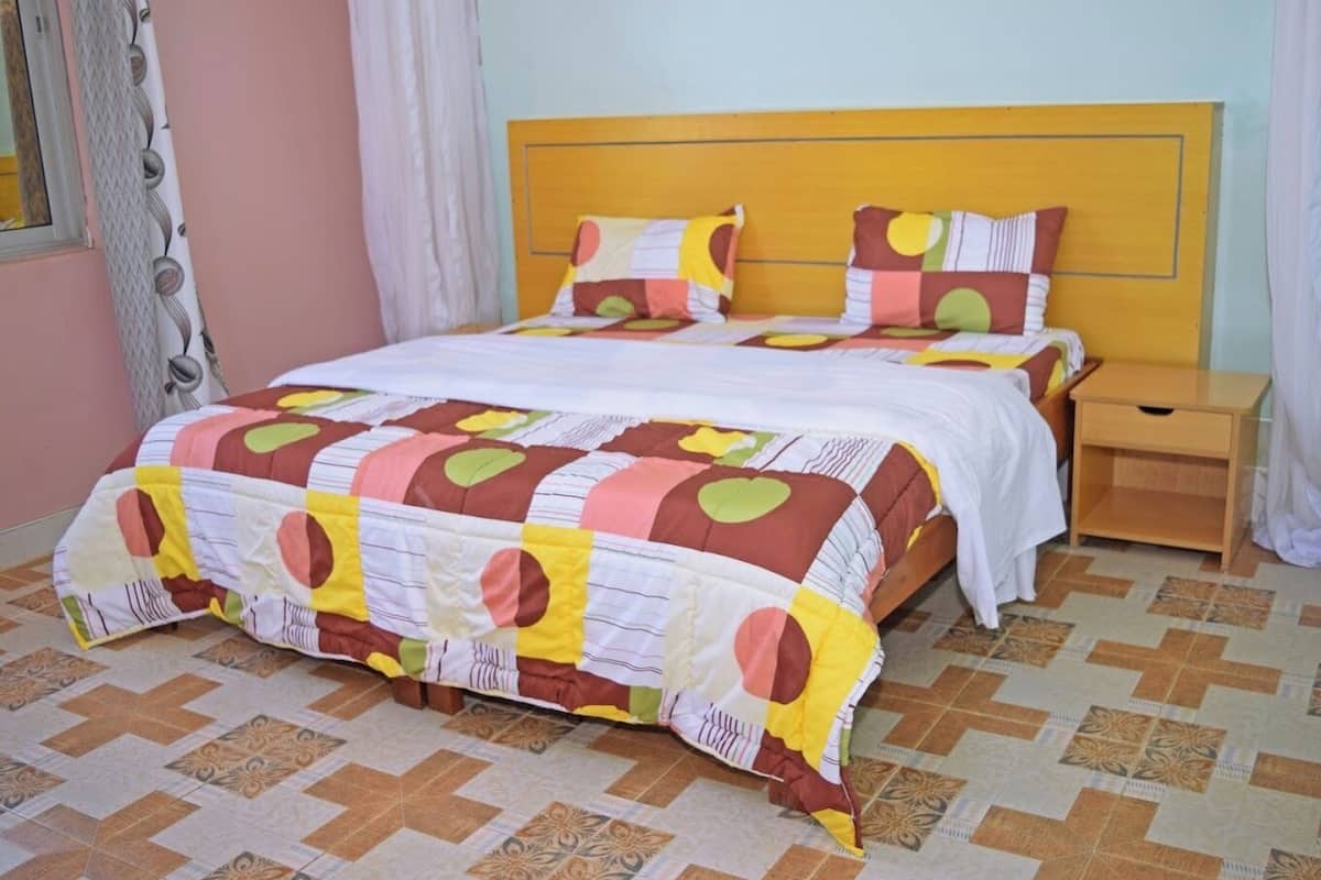 A bed with a colorful quilt, a wooden nightstand, and a patterned floor.