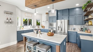Una cocina moderna con armarios azules, una isla grande, electrodomésticos de acero inoxidable e iluminación colgante.