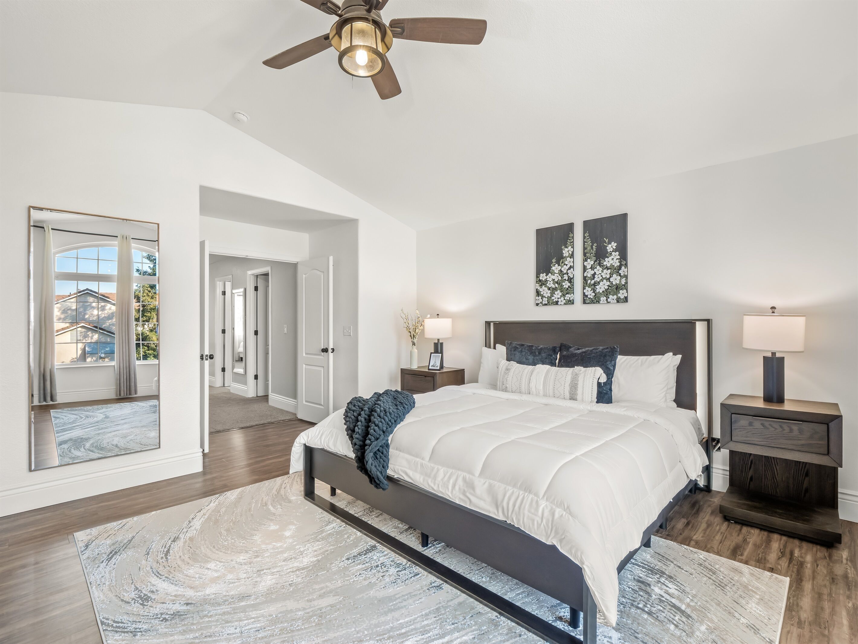 A bedroom with a bed, bedside tables, a ceiling fan, and artwork on the wall.
