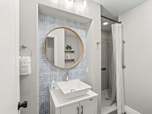 Un baño con un lavabo blanco, un espejo redondo y una zona de ducha.