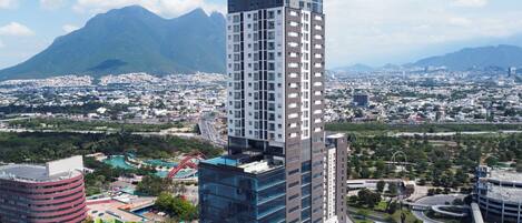 A high-rise building with a modern glass facade, surrounded by a cityscape and mountains in the background.