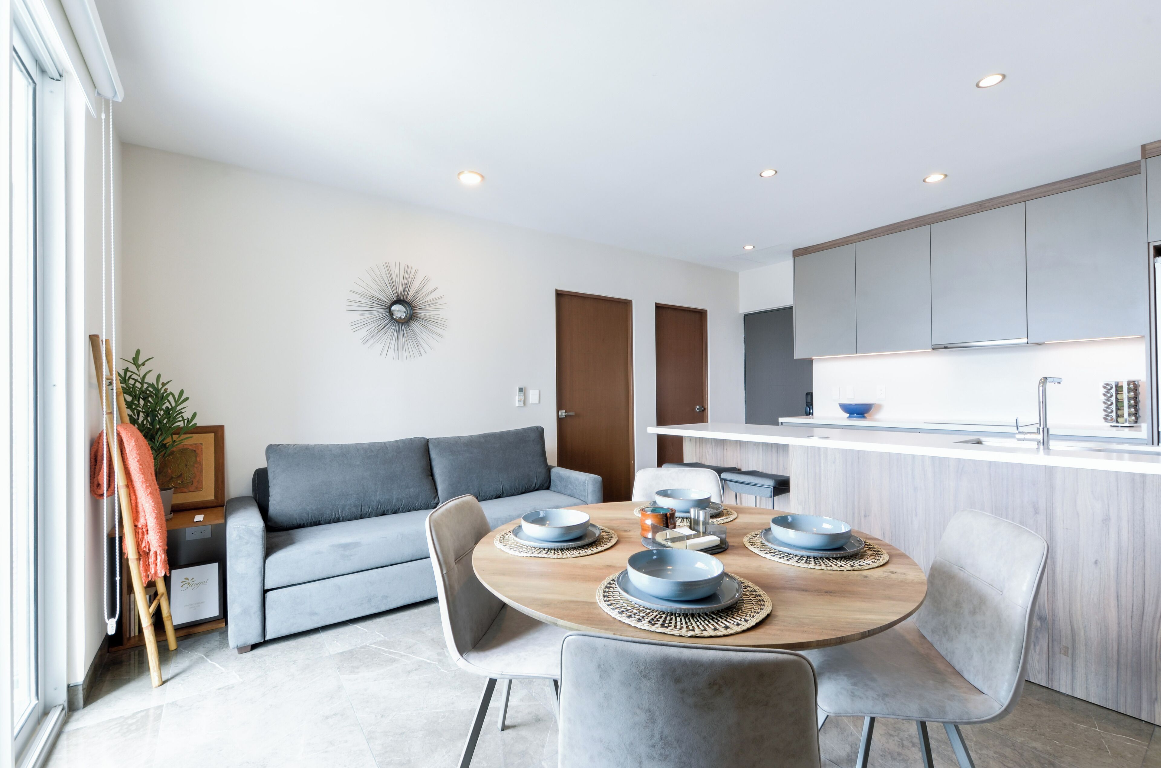 Una cocina moderna con armarios blancos, una mesa de comedor de madera con platos azules y un sofá gris.
