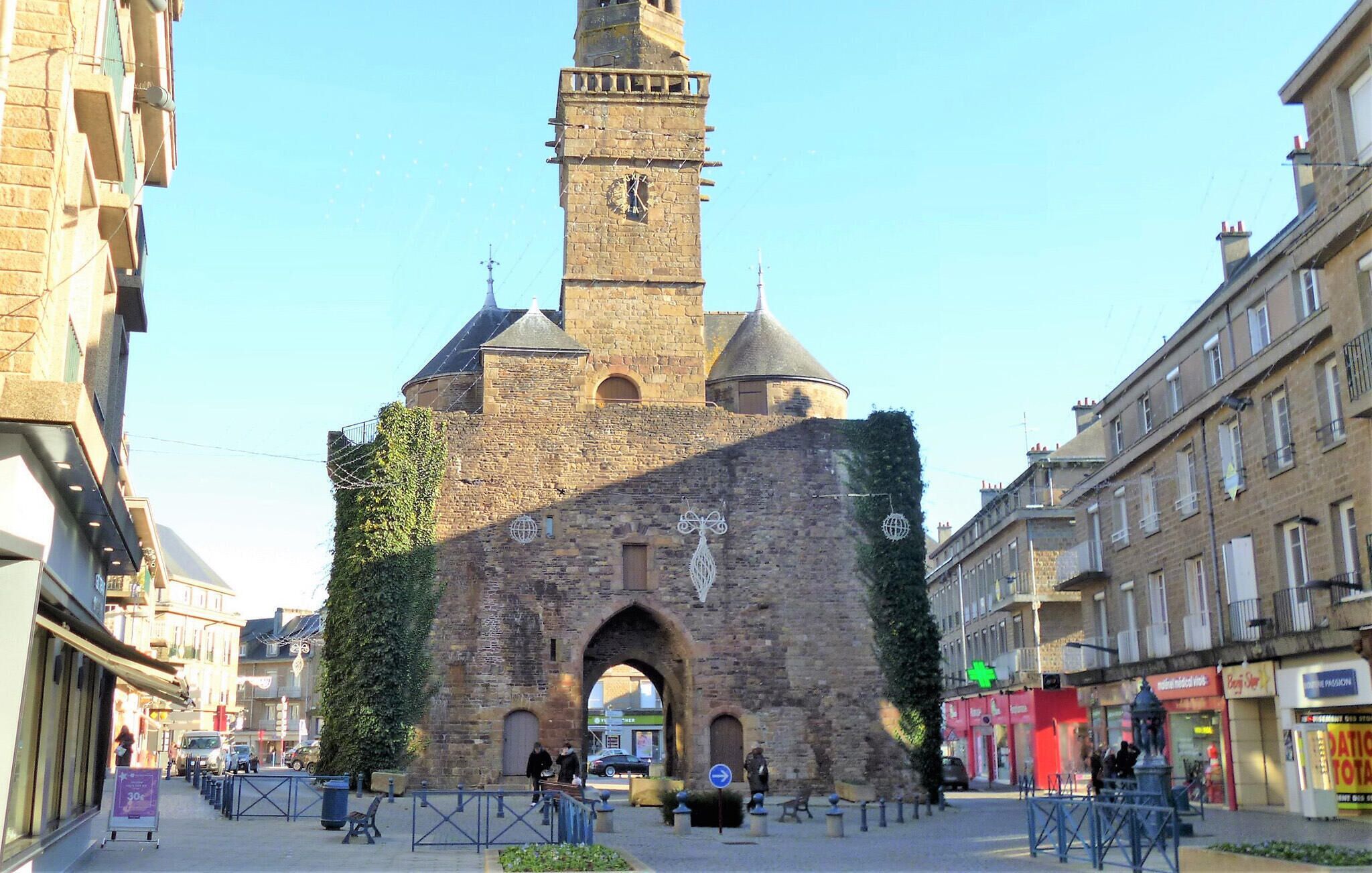 Ein historisches Steinhaus mit einem Uhrturm, einem Rundbogenportal und einer mit Efeu bewachsenen Fassade.