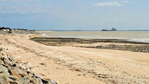 A sandy beach with a stone wall on one side and a rocky outcrop in the distance. - Belle location raffinée (Frênes, Tinchebray-Boc)