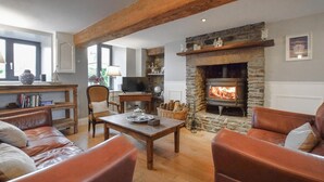 A cozy living room with a stone fireplace, leather sofas, a wooden coffee table, and a bookshelf. - Belle location raffinée (Frênes, Tinchebray-Boc)