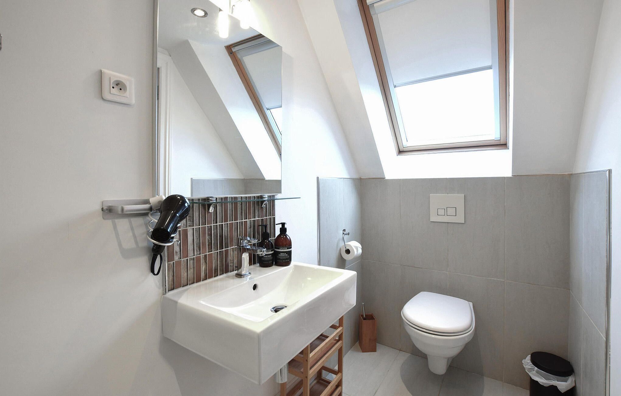 Un baño moderno con tragaluz, un lavabo blanco, un inodoro y un espejo.