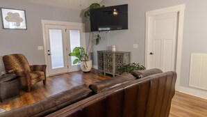 A living room with a brown leather sofa, a leopard print chair, a television mounted on the wall, and a small side table with a plant. - Perfect Masters Week Stay- Spacious Home ONLY 10 Miles from Augusta National (North Augusta)