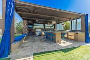 An outdoor kitchen area with a grill, bar stools, and a covered seating area. - Massive Estate, Pickle Ball, Splash Pad, Mini Golf (Cave Creek)