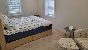 Een slaapkamer met een bed, twee ramen, een tafeltje en een stoel.