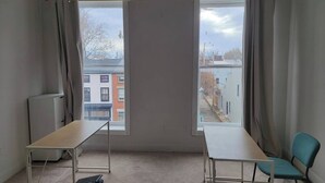 Een kamer met twee ramen, een tafel, een stoel en een radiator.