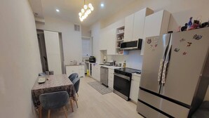 Een kleine keuken met een eettafel, stoelen, een koelkast, magnetron en een kookplaat.