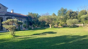 Un edificio in pietra con tetto in tegole, circondato da un prato curato e diversi alberi.