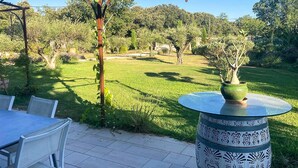 Una zona patio all'aperto con un tavolo rotondo e sedie, circondata da un prato curato e alberi.