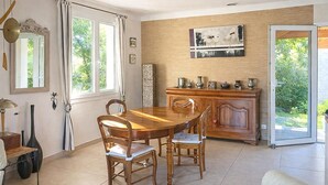 Zona pranzo con tavolo e sedie in legno, un armadietto contenente stoviglie e vista sul verde attraverso una porta vetrata.