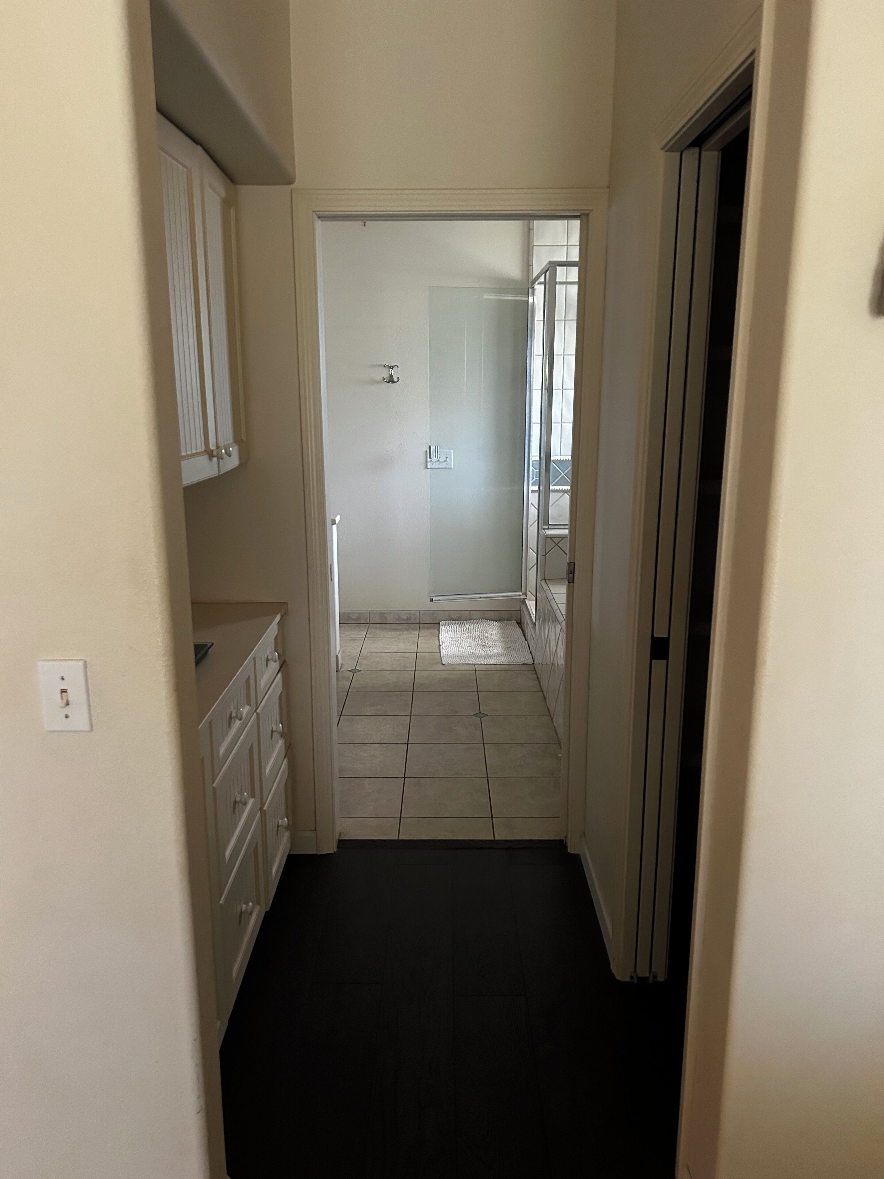 A narrow hallway with a tiled floor, a white door at the end, and a small window with a view of a balcony.