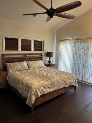 A bedroom with a wooden bed, a ceiling fan, a nightstand, a lamp, and a window with curtains. - Steps from the Beach! Exclusive 3/2.5 home in Poipu. Utilities Included! (Koloa)