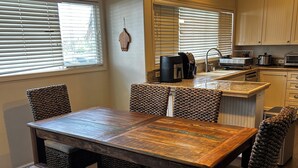 A dining area with a wooden table and chairs, a bench, a kitchen with a sink and appliances, and a hanging light fixture. - Steps from the Beach! Exclusive 3/2.5 home in Poipu. Utilities Included! (Koloa)