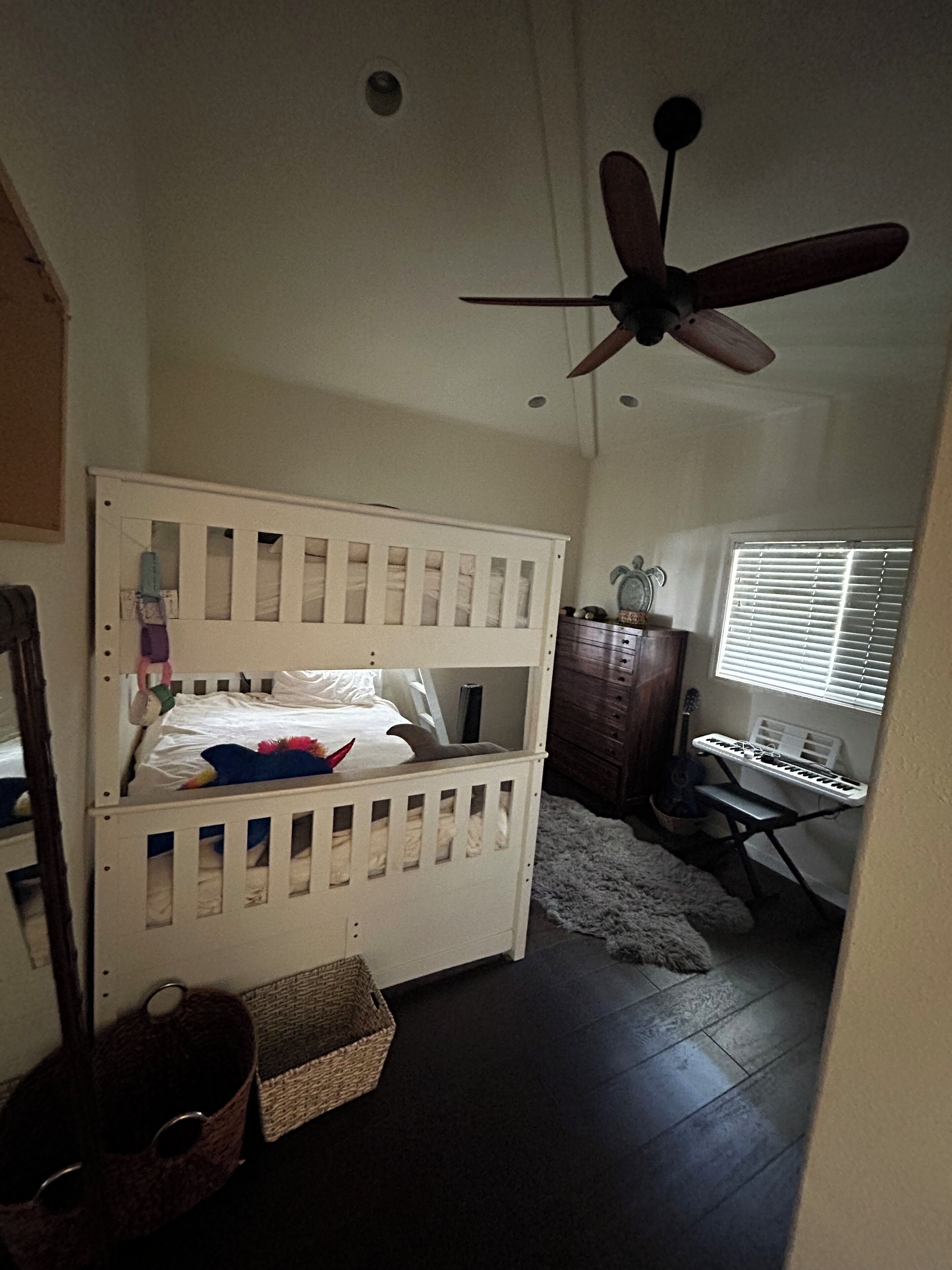 Habitación infantil con literas, ventilador de techo, ventana con persianas, un teclado y una guitarra.
