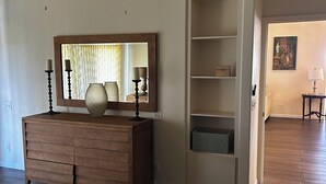 A bedroom with a wooden dresser, a large mirror, and a built-in shelving unit. - Steps from the Beach! Exclusive 3/2.5 home in Poipu. Utilities Included! (Koloa)