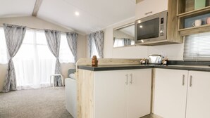 Eine moderne Küche mit weißen Schränken, einer Mikrowelle und einem Toaster. Es gibt eine Holz Arbeitsplatte und ein Fenster mit Vorhängen.