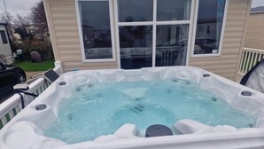 Ein Whirlpool mit weißer Außenhülle und schwarzen Akzenten, gelegen in einem Garten mit einem Haus im Hintergrund.