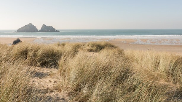 Ein Strand mit Dünen und zwei markanten Felsformationen in der Ferne.