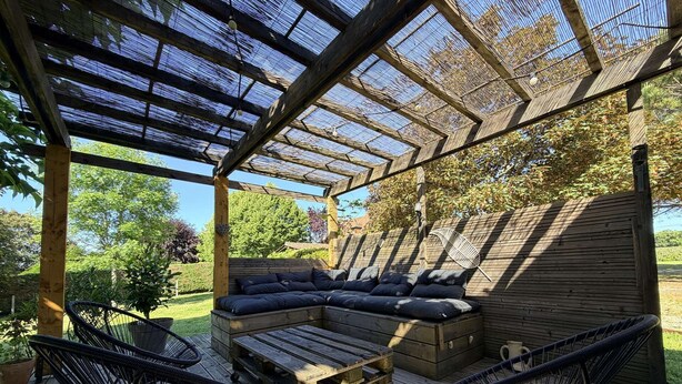 Een overdekt terras met een houten bank, twee stoelen en een bank.