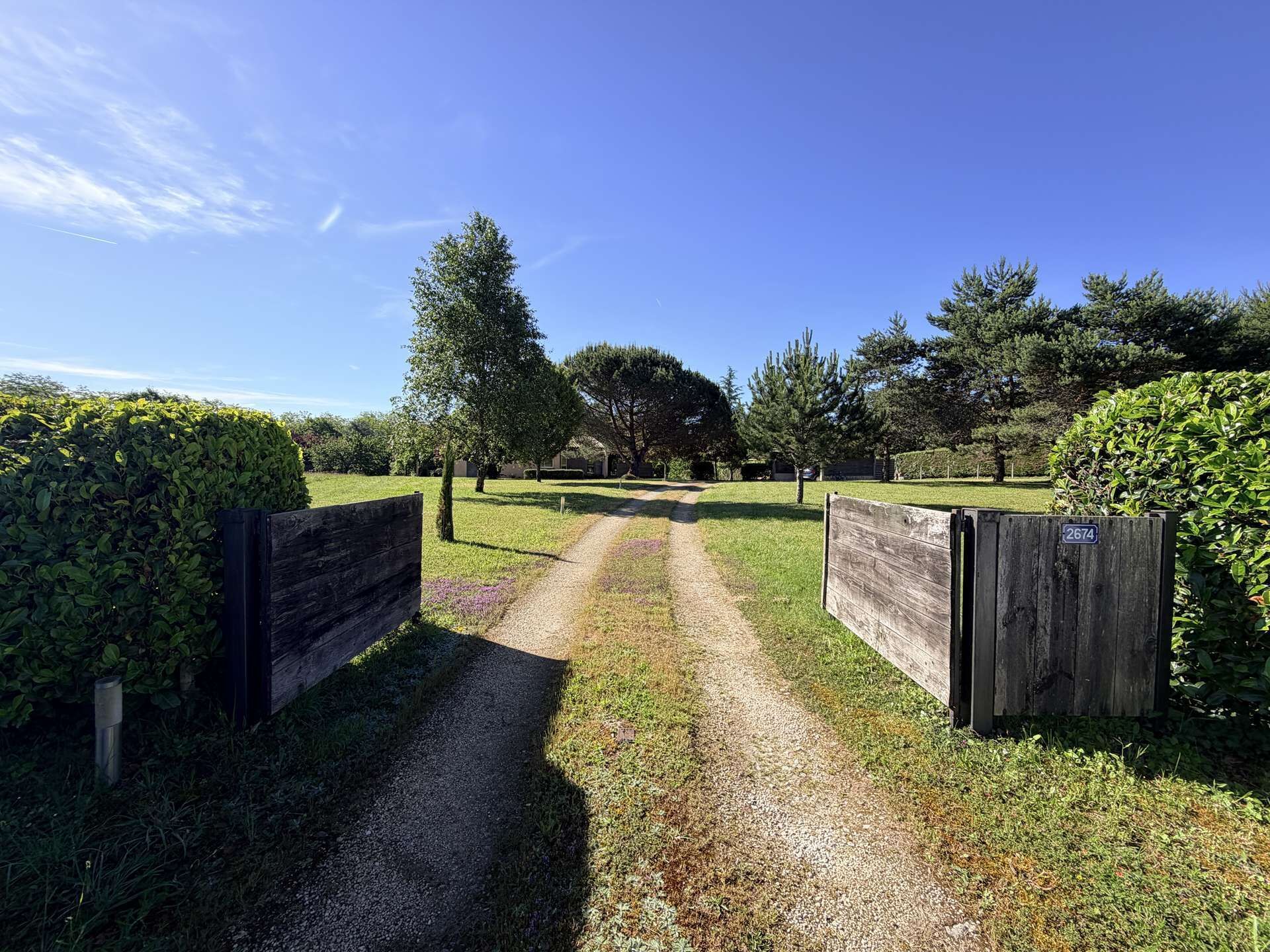 A gravel path leading through a fenced area with a wooden gate, surrounded by well-maintained grass and trees.