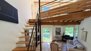 Een ruime woonkamer met een houten trap, een piano en een bank.