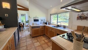 Een moderne keuken met houten kasten, een centraal eiland en een groot raam met uitzicht op de omgeving.