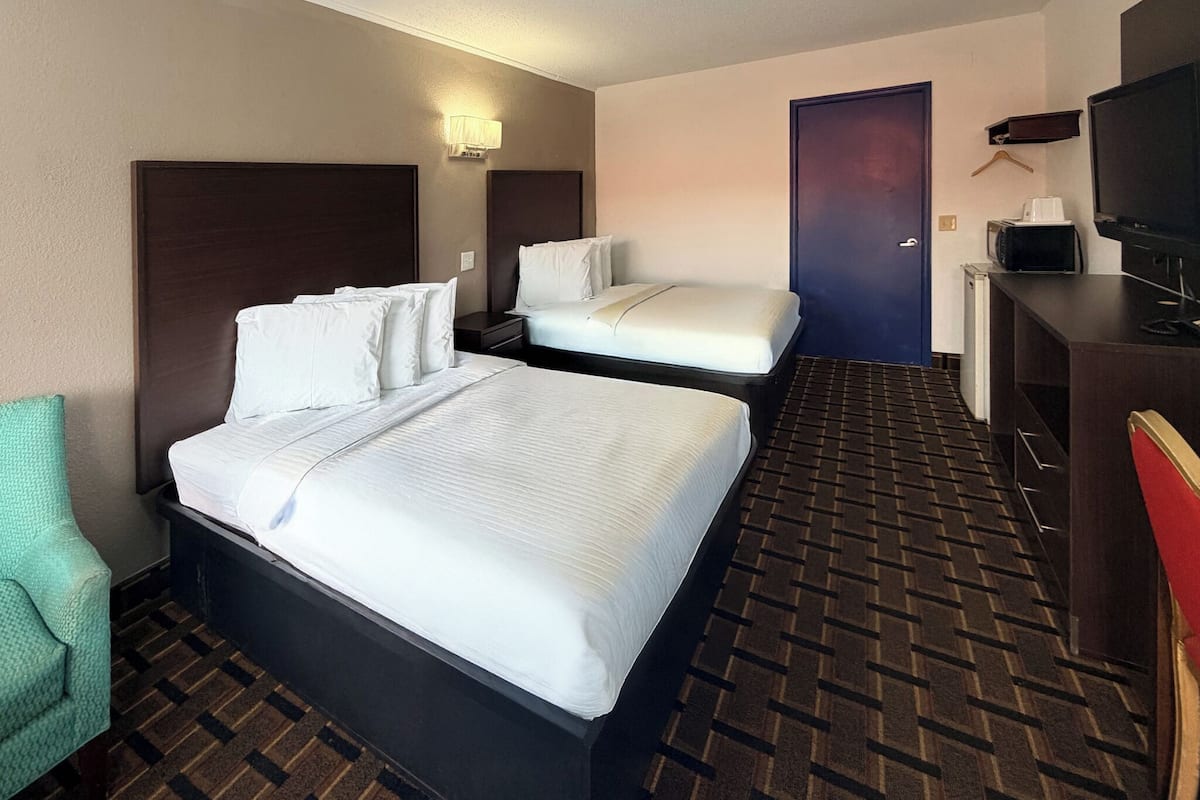 Habitación de hotel con una cama grande, otra más pequeña, un escritorio con televisor, un microondas y una silla.
