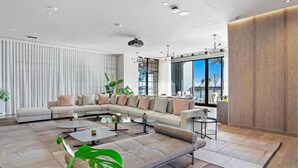 Un salon moderne avec un canapé d’angle, des tables basses et une grande fenêtre donnant sur l’extérieur.