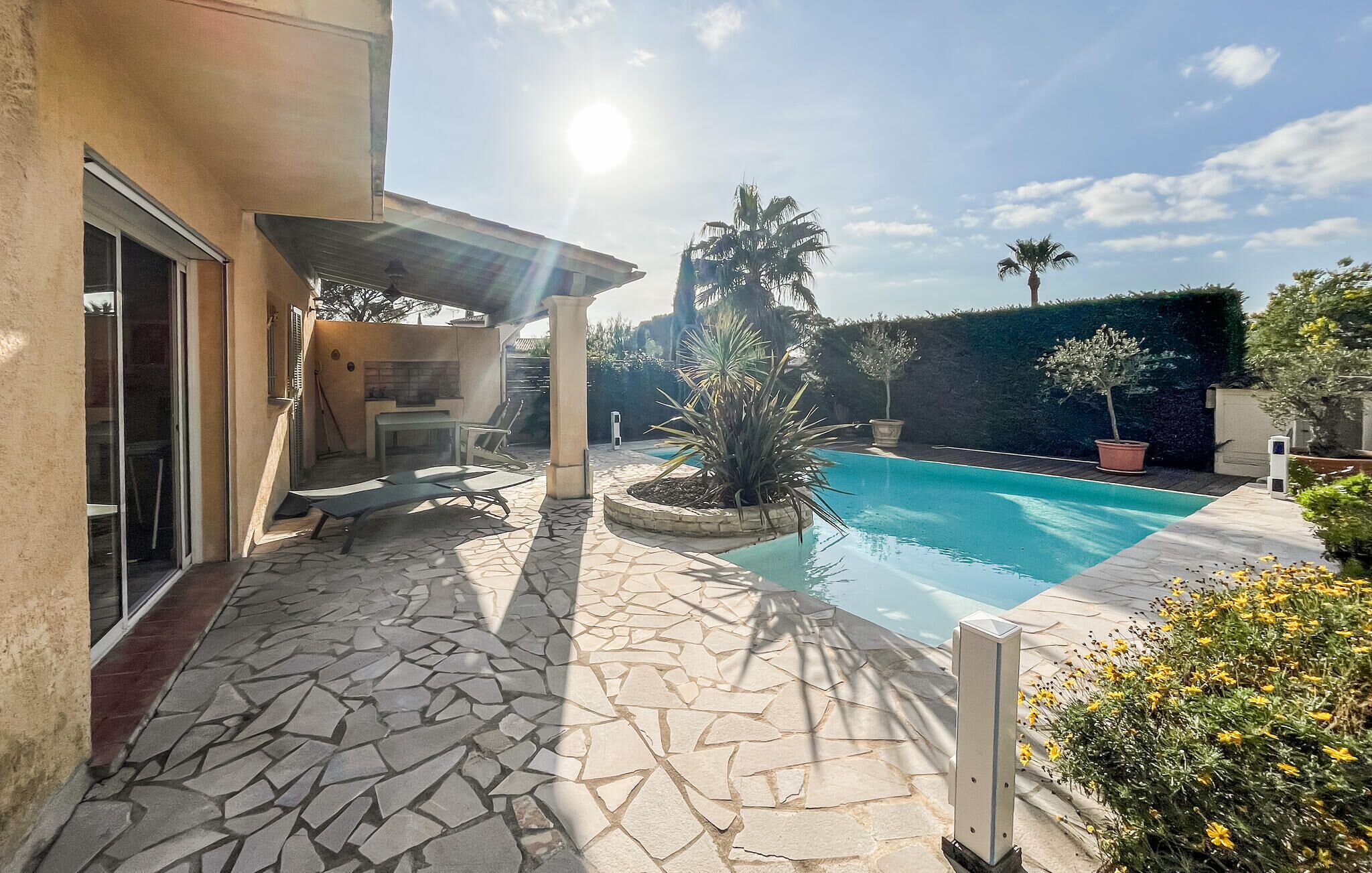 A poolside area with a stone patio, a pool, and a covered seating area with a table and chairs.