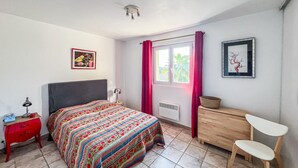 Une chambre à coucher comprenant un lit, une table de chevet, une chaise, une commode, une fenêtre avec des rideaux et un ventilateur de plafond.