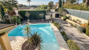 Une piscine entourée d’un jardin où poussent différentes espèces de plantes, ainsi que d’une terrasse en bois.