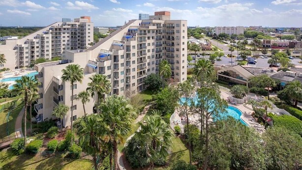 Un hotel moderno de altura con varios balcones, piscina y exuberante vegetación.