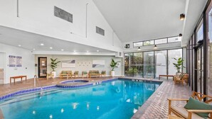 Una piscina interior con agua azul cristalina, rodeada de sillas de descanso de madera y un suelo de baldosas.