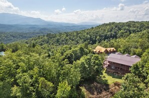 A lodge with a red roof nestled in a forested area with a view of distant mountains. - 6 BR, large indoor pool, full arcade, views, cinema, and gameroom. Sleeps 25+ (Pittman Center)
