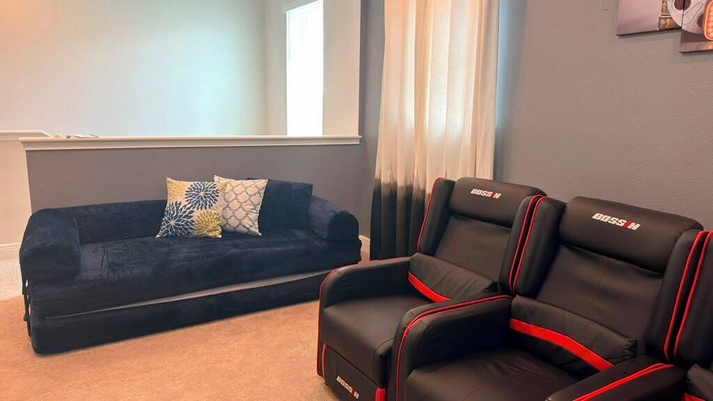 Una habitación con un sofá oscuro y dos sillas de carreras negras y rojas.