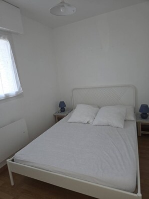 A single-bed room with a white bed, two bedside tables with lamps, a window with sheer curtains, and a white ceiling light. - Ideal apartment for 2/3 people with sea view (DAMGAN)