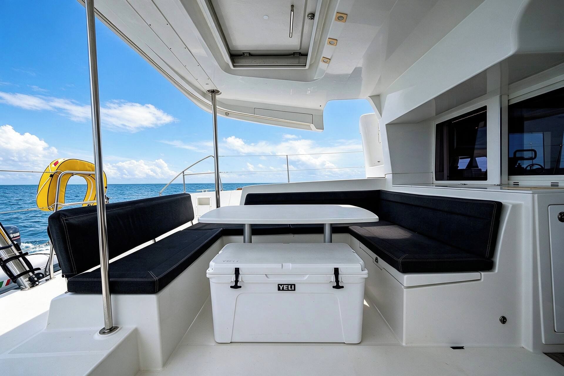 A boat's interior with a seating area, a table, a cooler, and a window.