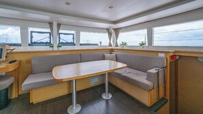 A compact living space with a sofa, a small table, and a window overlooking a body of water. - 46ft Catamaran · 4 Ensuite Cabins · Pool & Beach (Key West)