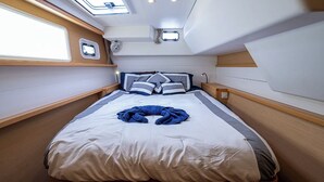 Une cabine compacte et bien éclairée, dotée d’un lit simple agrémenté d’une serviette bleue, de lambris en bois et de petites fenêtres.