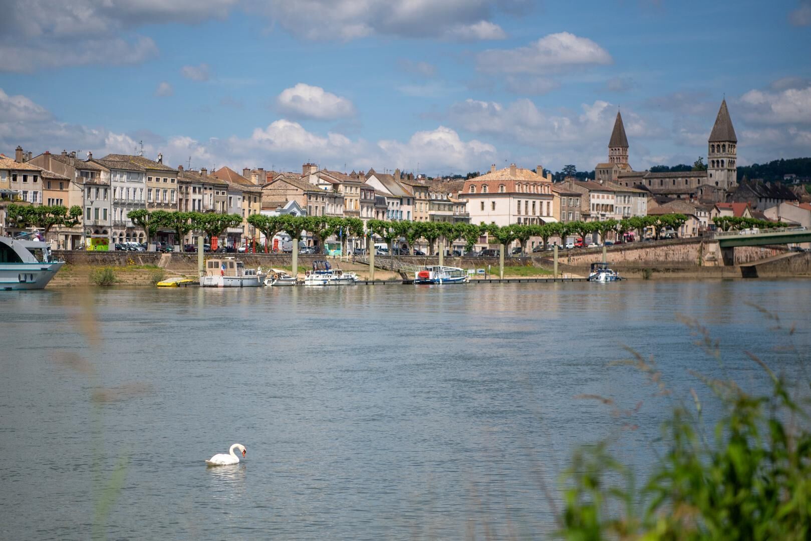 Une rivière où l’on peut voir des bateaux et des cygnes, un pont et des bâtiments historiques, dont une tour imposante.