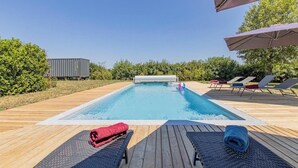 En pool med en träbrygga, solstolar och ett överbyggt område.