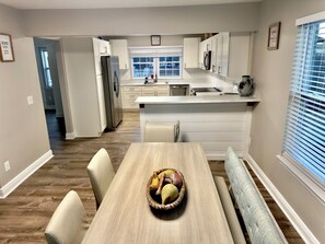 Una cocina moderna con armarios blancos, un refrigerador de acero inoxidable y una zona de comedor con una mesa y sillas de madera.