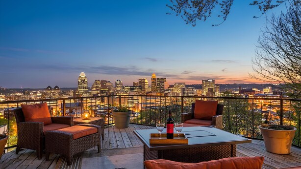 Eine Dachterrasse mit Korbmöbeln, einem Tisch mit Flasche und Gläsern sowie Blick auf eine Stadtlandschaft.