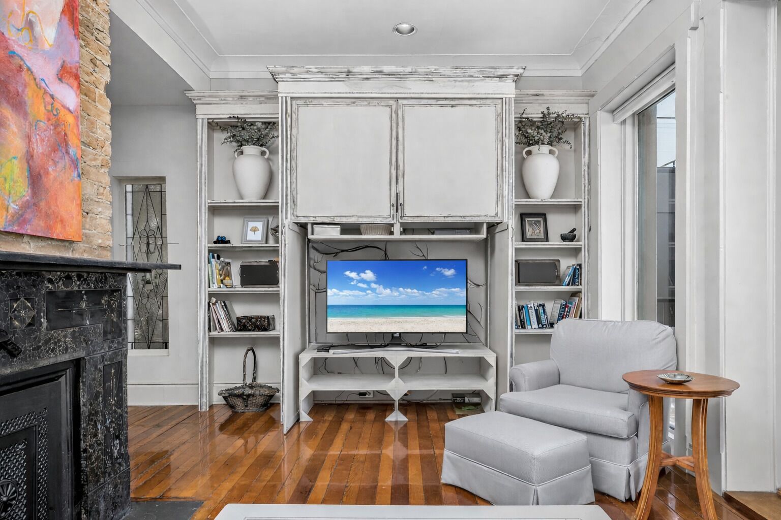 A living room with a fireplace, a television on a white entertainment unit, a grey sofa, and a small wooden side table.