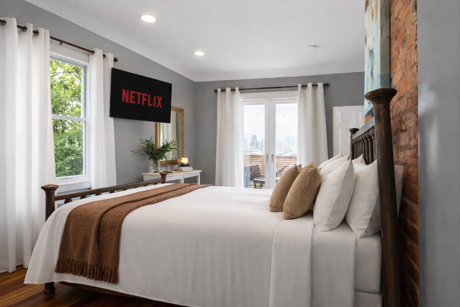 A bedroom with a bed, a TV mounted on the wall, a window, and a view of the city.
